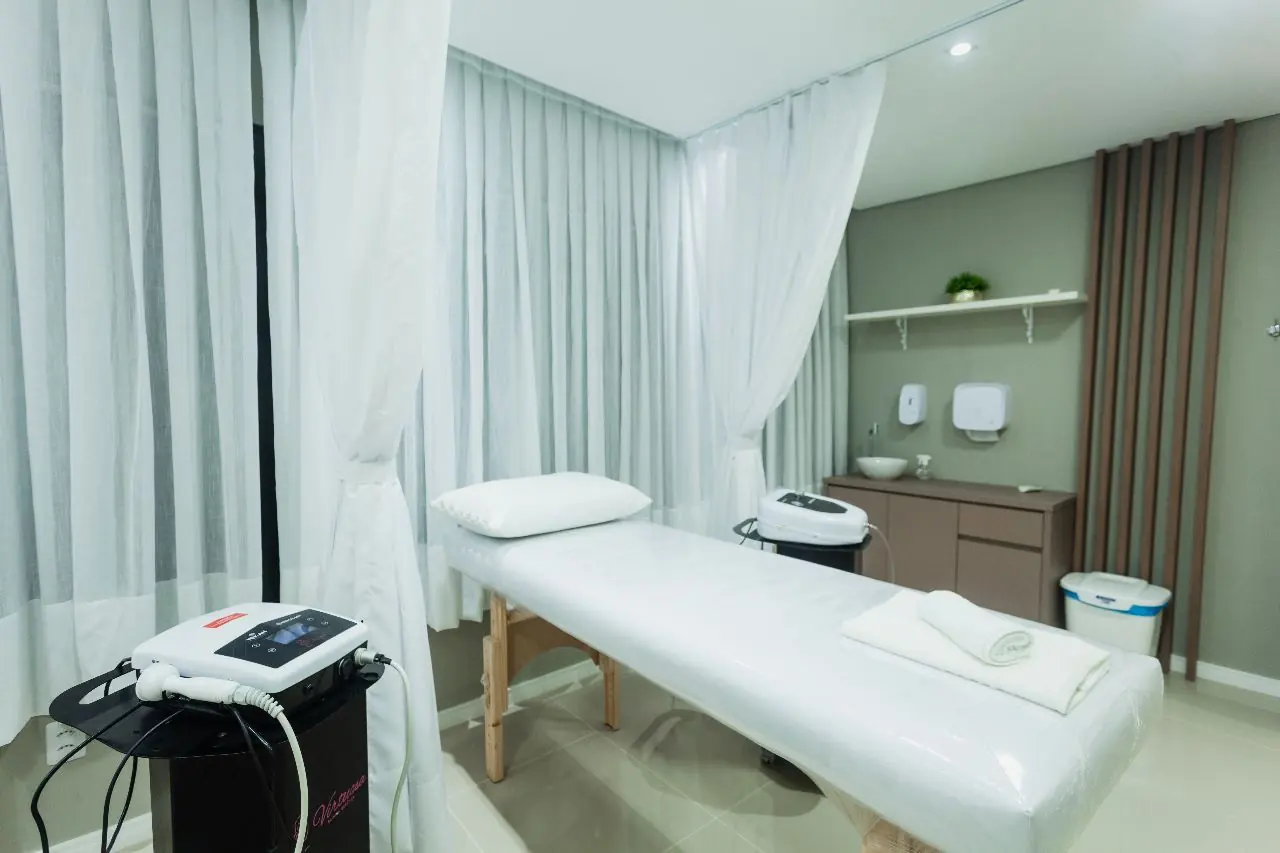 Cabine corporal da Virtuosa Belém, com maca, cortinas brancas e aparelho